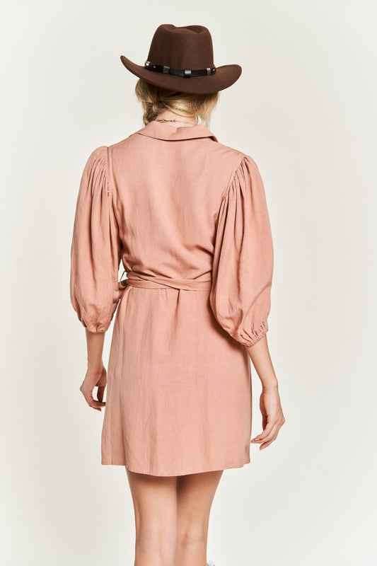 Back view of a plus size button down dress in soft pink with puff sleeves and a tied waist