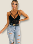 Stylish black lace bodysuit for women featuring crisscross straps and a sheer design, paired with ripped jeans